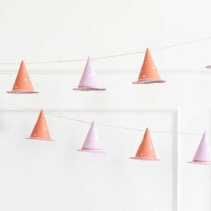 May include: A string of witch hat party decorations with alternating pink and orange hats with white stars. The hats are strung on a white string.