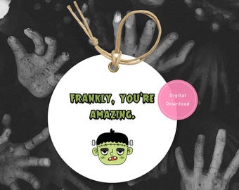 May include: A white, round tag with the text "Frankly, You're Amazing" in green and a cartoon Frankenstein's monster. A pink circle with "Digital Download" is on the right. The tag has a brown string and is set against a background of zombie hands.