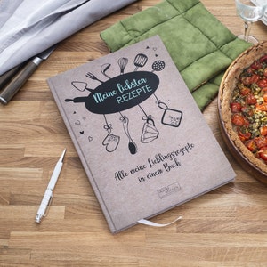 Könnte beinhalten: Ein braunes Kochbuch mit dem Titel "Meine liebsten REZEPTE" und dem Text "Alle meine Lieblingsrezepte in einem Buch". Das Cover zeigt eine handgezeichnete Illustration von Küchenutensilien und einem Herzen.