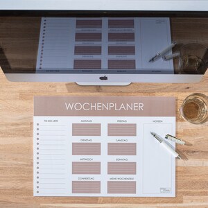 Könnte beinhalten: Ein brauner Wochenplaner mit einer To-Do-Liste, Platz für tägliche Aufgaben und einem Bereich für wöchentliche Ziele. Der Planer hat ein schlichtes Design mit weißem Text und Linien.