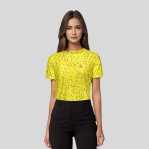 A woman wearing the yellow sprinkle golf polo shirt and black trousers, viewed from the waist up.