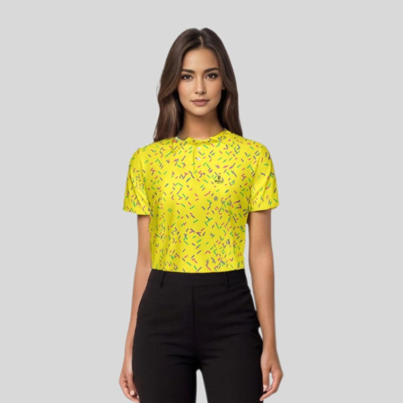 A woman wearing the yellow sprinkle golf polo shirt and black trousers, viewed from the waist up.