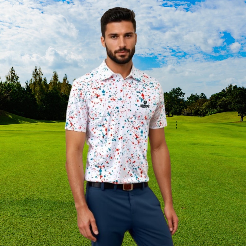A man standing on a golf course wearing the white paint splatter polo shirt and blue trousers.