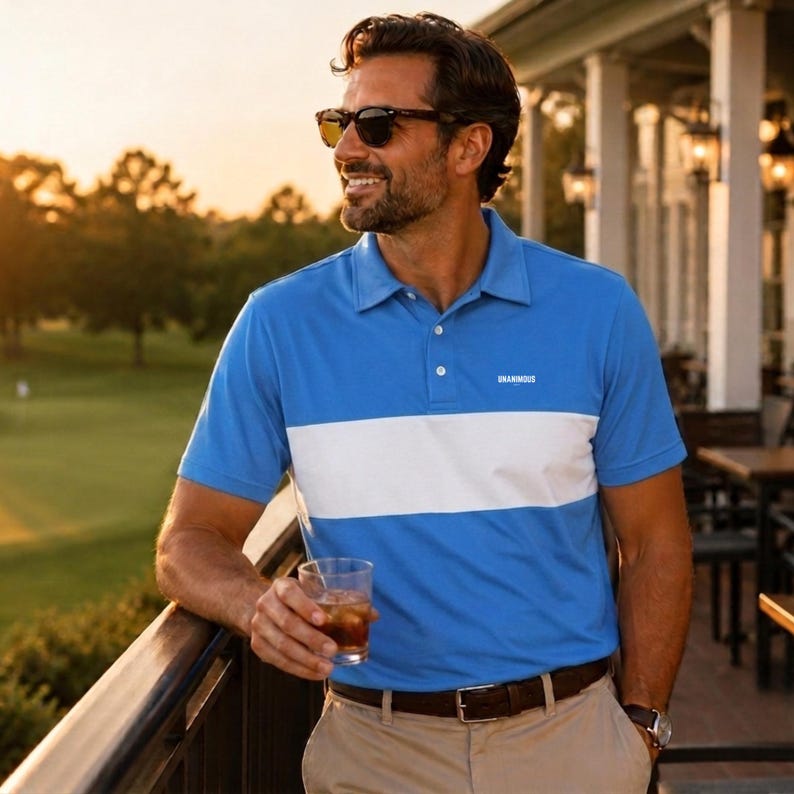 Smiling man in sunglasses leaning on a clubhouse rail at golden hour, wearing a Unanimous Golf powder blue polo with a white chest stripe and tan chinos.