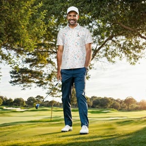 Full-body view of a man holding a golf club on a green course, wearing a white polo shirt and dark pants.