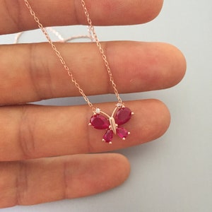 Puede incluir: Un delicado collar de oro rosa con un colgante de mariposa con detalles de piedras preciosas rojas.