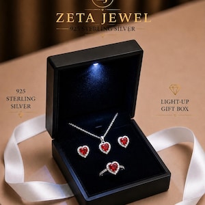 May include: A 925 sterling silver jewelry set featuring a heart-shaped red stone necklace, matching heart-shaped stud earrings, and a heart-shaped ring, all displayed in a black light-up gift box labeled ZETA JEWEL 925 STERLING SILVER.