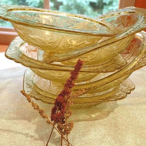 May include: A stack of amber-colored glass bowls with a floral design. The bowls have a scalloped edge and are stacked on top of each other. A few sprigs of dried flowers are in the foreground.