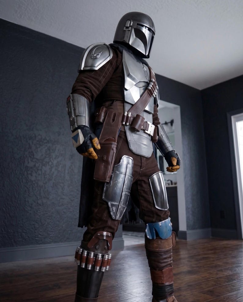 May include: A full-body shot of a Mandalorian costume. The costume features a silver helmet, chest plate, and arm guards over a brown and gray jumpsuit. Brown leather accents include a belt, holster, and boot details. The costume is designed with a futuristic aesthetic.