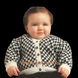 May include: A baby wearing a black and white checkered pattern cardigan sweater with a cream-colored collar and cuffs. The sweater has black buttons down the front. The baby is looking directly at the camera.