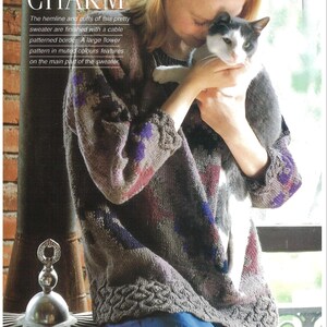 May include: A gray sweater with a cable patterned border and a large flower pattern in muted colors. The text "RUSTIC CHARM" is at the top of the image. A person is holding a gray and white cat.
