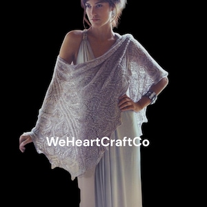 May include: A light gray, open-weave shawl with intricate lace patterns. The shawl is draped over the shoulders, with the text "WeHeartCraftCo" visible on the lower left side. The shawl appears to be made of a soft, possibly wool, material.
