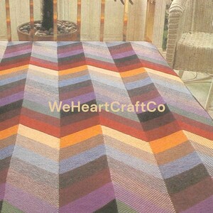 May include: A colorful, chevron-patterned blanket in shades of orange, red, purple, blue, and gray. The blanket has a textured appearance and the text "WeHeartCraftCo" is visible. The blanket is likely handmade and suitable for home decor.