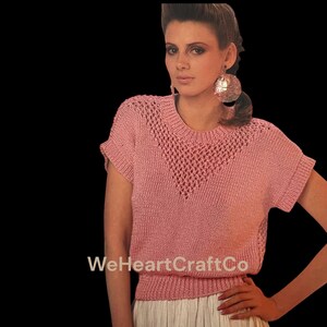 May include: A vintage pink knitted top with an openwork design on the upper chest. The short-sleeved top has a ribbed hem and a round neckline. The image includes the text "WeHeartCraftCo".