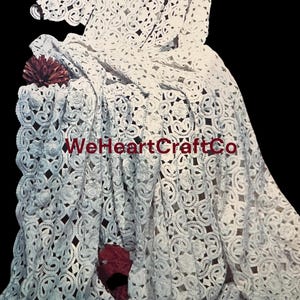 May include: White lace fabric with a floral pattern. The fabric is draped, with a dark background. The text "WeHeartCraftCo" is visible on the fabric. A dark red flower is placed on the fabric.