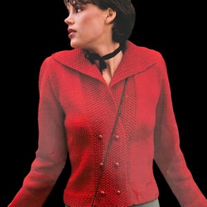 May include: A red knitted cardigan with a large collar, double breasted closure, and four buttons. The cardigan has a textured knit pattern.