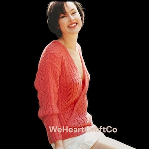 May include: A coral-colored, knitted wrap sweater with a deep V-neck. The sweater features a textured, open-knit design and three-quarter sleeves. The image includes the text "WeHeartCraftCo" at the bottom.