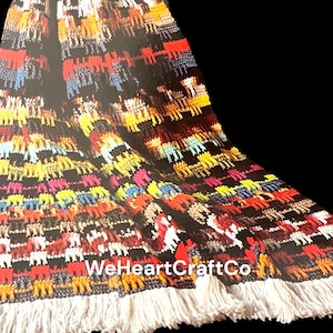 May include: A black textile with a colorful pattern of animal figures in red, yellow, blue, and pink. The textile has a white fringe along the bottom edge. The text "WeHeartCraftCo" is visible.