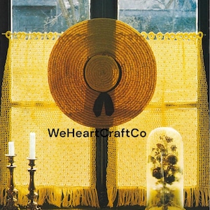May include: A straw sun hat with a black ribbon is centered in front of a yellow crocheted curtain. Two brass candle holders with white candles are on the left. A glass cloche with dried flowers is on the right. The text "WeHeartCraftCo" is visible.