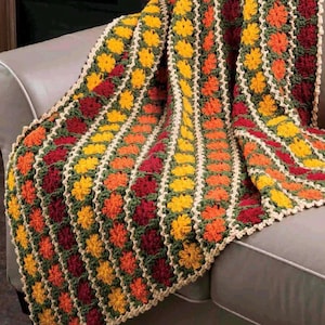 Peut inclure: Une couverture au crochet faite à la main, drapée sur un canapé. La couverture présente un motif floral aux tons de jaune, orange, rouge et vert, avec une bordure crème. Cette couverture douillette est parfaite pour ajouter de la chaleur et du style à tout espace de vie.