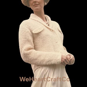 May include: Cream-colored, textured knit jacket with a collared neckline and two small front pockets. The jacket is buttoned and worn over a matching skirt. The image includes the text "WeHeartCraftCo".