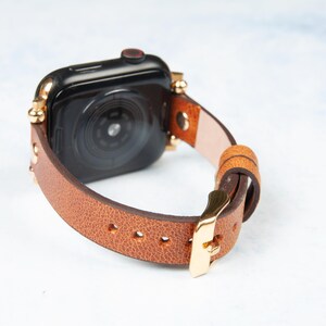 May include: A brown leather watch band with gold-colored accents and a gold buckle. The watch face is black. The band is made of a light brown leather and is secured with a gold-colored buckle.