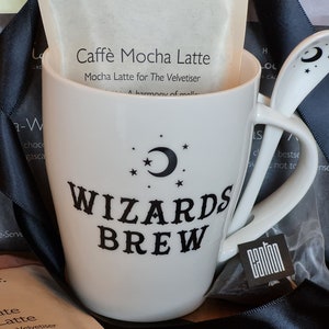 May include: White ceramic mug with a black and white design that says "Wizards Brew" and a crescent moon with stars. The mug is sitting on a black surface with a white and black package that says "Caffè Mocha Latte" and "Mocha Latte for The Velvetiser".