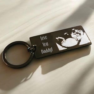 Op de afbeelding: Zwarte metalen sleutelhanger met een zilveren gegraveerd beeld van een echo en de tekst "Love You Daddy!"