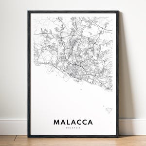 Può includere: Stampa con cornice nera raffigurante una mappa in bianco e nero di Malacca, Malesia. Il nome della città è stampato in un carattere moderno sotto la mappa. La mappa mostra la rete stradale e le caratteristiche geografiche.