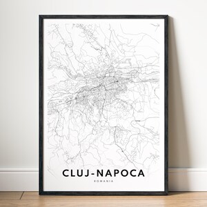 May include: A framed black and white map print of Cluj-Napoca, Romania. The detailed city map features a network of roads and streets, with the city name and country printed in a clean, modern font at the bottom.