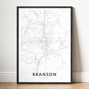 May include: A framed black and white map print of Branson, Missouri. The map details the city's roads, waterways, and buildings. The city name and state are printed in a clean, sans-serif font at the bottom of the print.