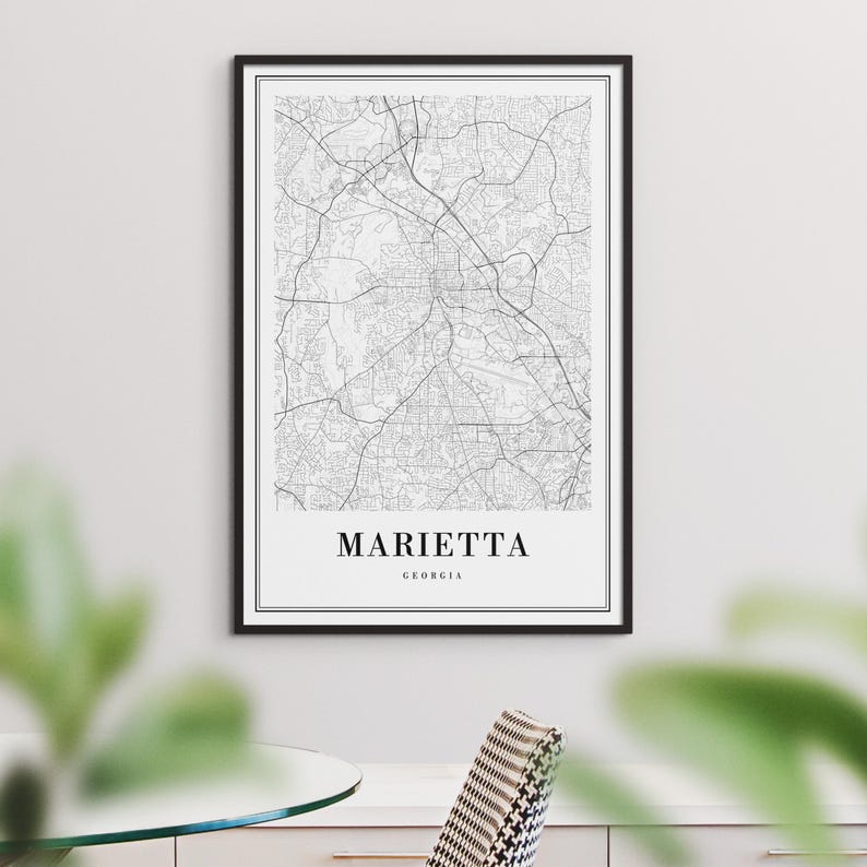 May include: A black and white map print of Marietta, Georgia, in a black frame. The map shows the city's streets and roads.