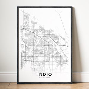 May include: Black framed print of a detailed map of Indio, California. The map is rendered in black lines on a white background, showcasing streets and infrastructure. The city name is displayed in a bold, sans-serif font at the bottom.