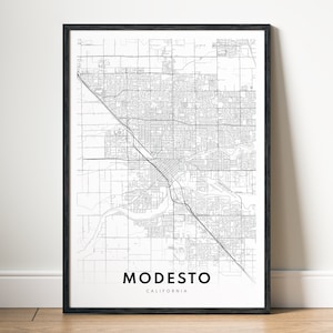 May include: A framed black and white map print of Modesto, California. The map details the city's streets and waterways. The city name is printed in a bold, sans-serif font at the bottom of the print.