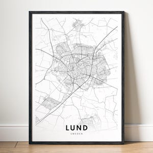 May include: A framed monochrome map print of Lund, Sweden. The map features a detailed network of streets and buildings. The city name and country are printed in a minimalist font at the bottom of the print, set within a black frame.