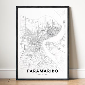 Peut inclure: Une impression d'art murale encadrée présentant un plan de ville en noir et blanc de Paramaribo, au Suriname. La carte affiche un réseau détaillé de rues et une rivière traversant la ville. Le texte PARAMARIBO et SURINAME est imprimé en noir.