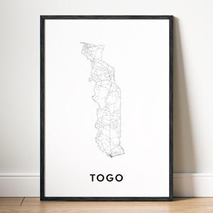 以下が含まれることがあります： 白い壁に黒い額縁に入った、トーゴの白黒の線画地図。地図は詳細で、国の道路と国境を示しています。地図の下には黒い文字で「TOGO」と印刷されています。