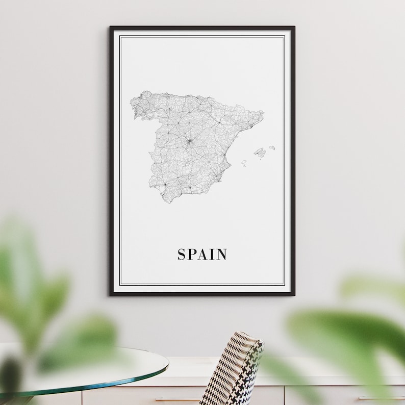 May include: A black and white line art map of Spain with the word "SPAIN" printed below the map. The map is framed in a black frame and is hanging on a white wall.