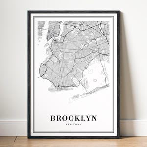 May include: A framed black and white map print of Brooklyn, New York. The map details the city's streets and waterways. The word "BROOKLYN" is printed in a bold font, with "NEW YORK" below it. The print is in a black frame.