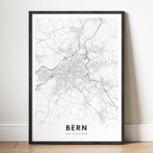 Puede incluir: Una impresión enmarcada en blanco y negro del mapa de Berna, Suiza. El mapa detallado muestra las carreteras y vías fluviales de la ciudad. El nombre de la ciudad y el país están impresos en una fuente limpia y moderna en la parte inferior.
