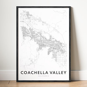 May include: Black framed print of the Coachella Valley, California, map. The map is a detailed black and white illustration of the area's roads and infrastructure. The words "COACHELLA VALLEY CALIFORNIA" are printed in a bold, black font at the bottom.