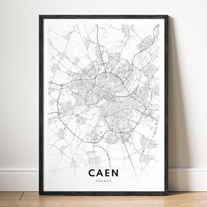 Può includere: Una stampa di mappa di Caen, Francia, in bianco e nero. La mappa è incorniciata in una cornice nera e il nome della città è stampato sotto la mappa.
