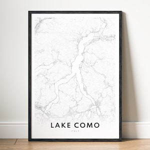 May include: Black framed print featuring a detailed, grayscale map of Lake Como, Italy. The lake's shape and surrounding areas are depicted with fine lines. The words "LAKE COMO" and "ITALY" are printed in a clean, sans-serif font at the bottom.