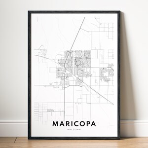 May include: A framed print with a black border, displaying a detailed map of Maricopa, Arizona. The map is in black lines on a white backdrop, with the city and state name below. The artwork is presented on a wooden floor.