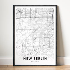 Op de afbeelding: Een ingelijste zwart-wit kaartprint van New Berlin, Wisconsin. De gedetailleerde kaart toont de straten en infrastructuur van de stad. De naam van de stad is gedrukt in een vetgedrukte, schreefloze letter onderaan de print.