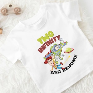Puede incluir: Camiseta blanca con un gráfico de Buzz Lightyear y Woody de Toy Story. El texto en la camiseta dice "Two Infinity and Beyond!"