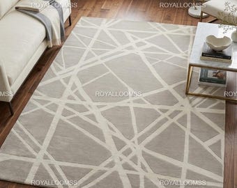 Alfombra de lana moderna con diseño geométrico abstracto, tejida a mano, en tonos beige y marfil, ideal para sala de estar.