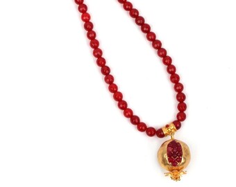 May include: A red beaded necklace with a gold pomegranate pendant. The pendant has red gemstones inside.