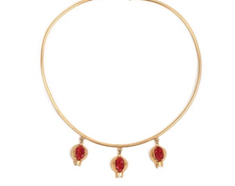 May include: A gold choker necklace with three dangling red pomegranate charms.