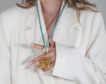 May include: A turquoise rope necklace with a large gold heart pendant adorned with turquoise and white stones.